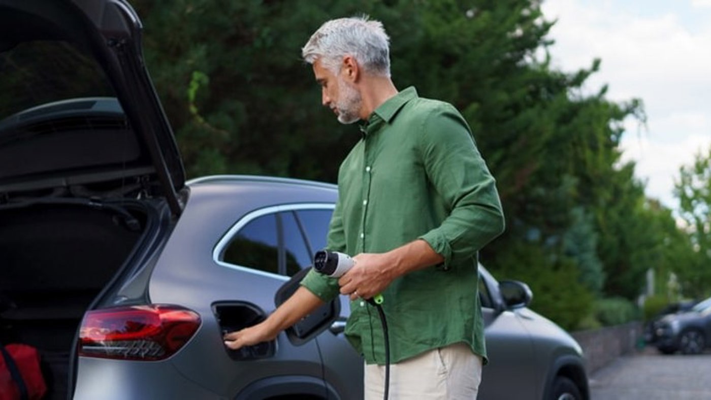 Man standing up and preparing to plug in EV charging cable to vehicle