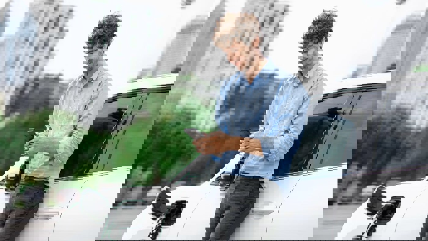 young man looking at mobile phone whilst electric vehicle charges