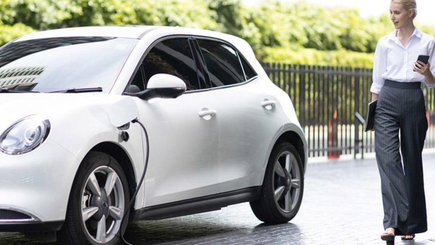 Woman walking with mobile phone while charging her EV at station