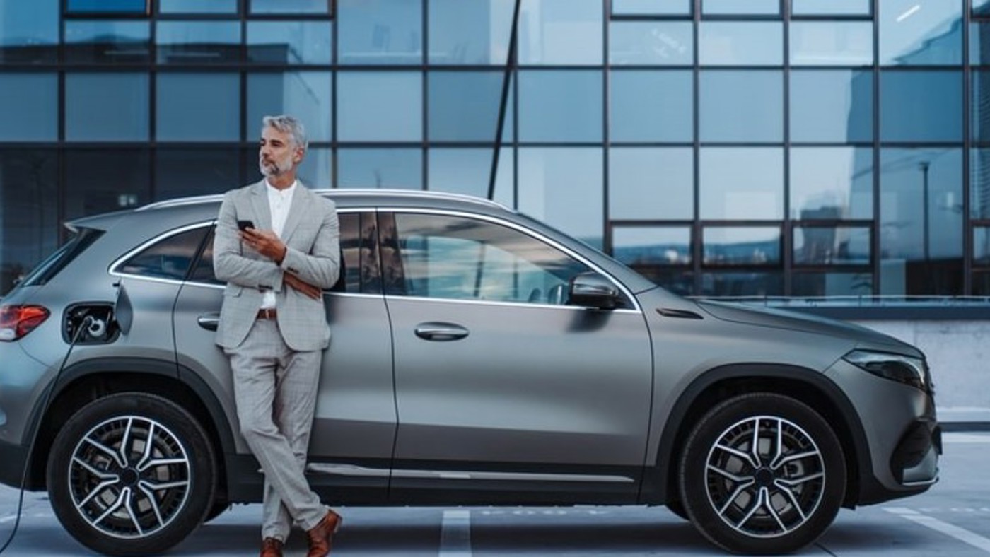 A businessman standing next to his charging EV.
