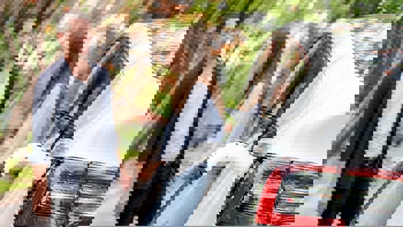 man and woman standing talking to eachother outdoors while EV car is charging