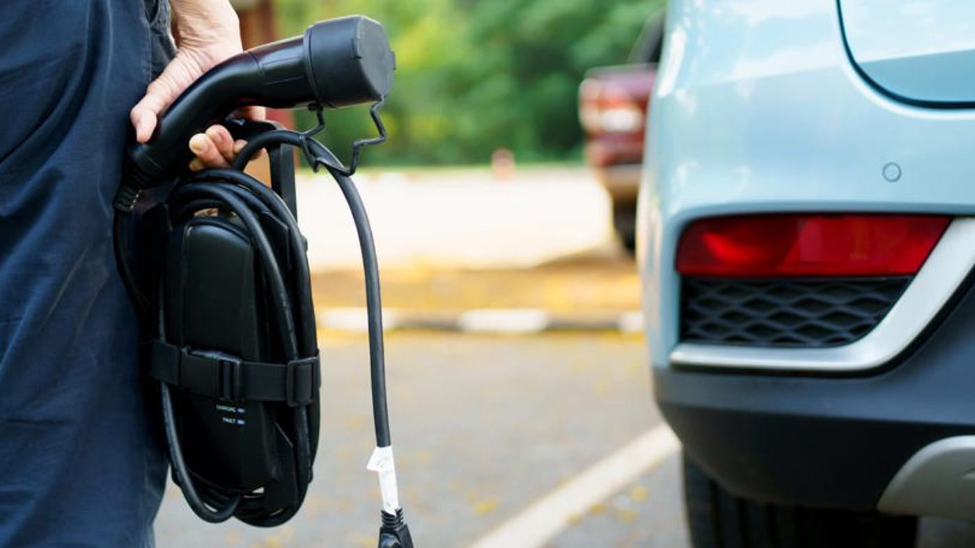 Shot of person carrying EV charger towards their electric car.