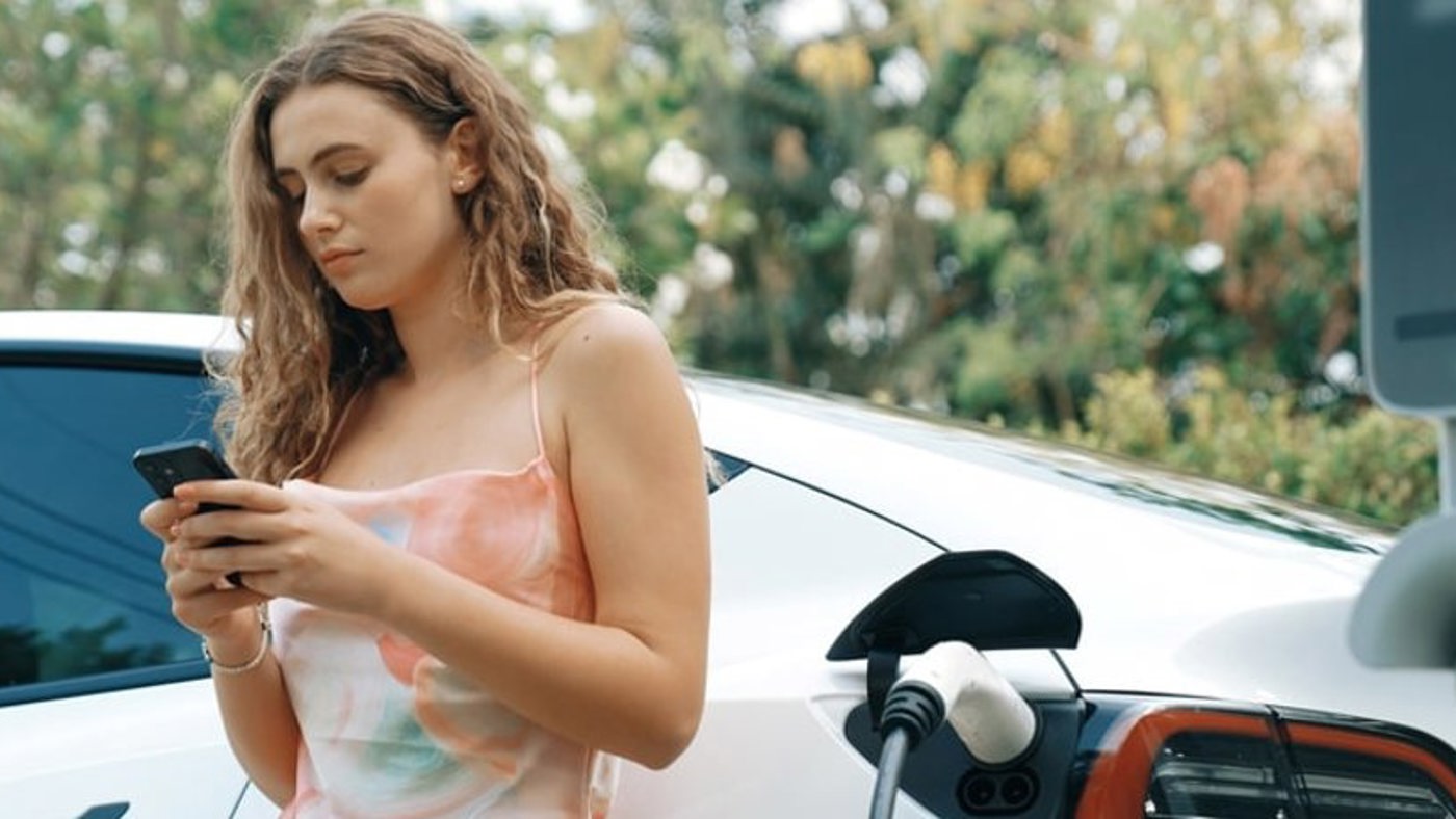Woman checking her phone for EV news whilst charging.
