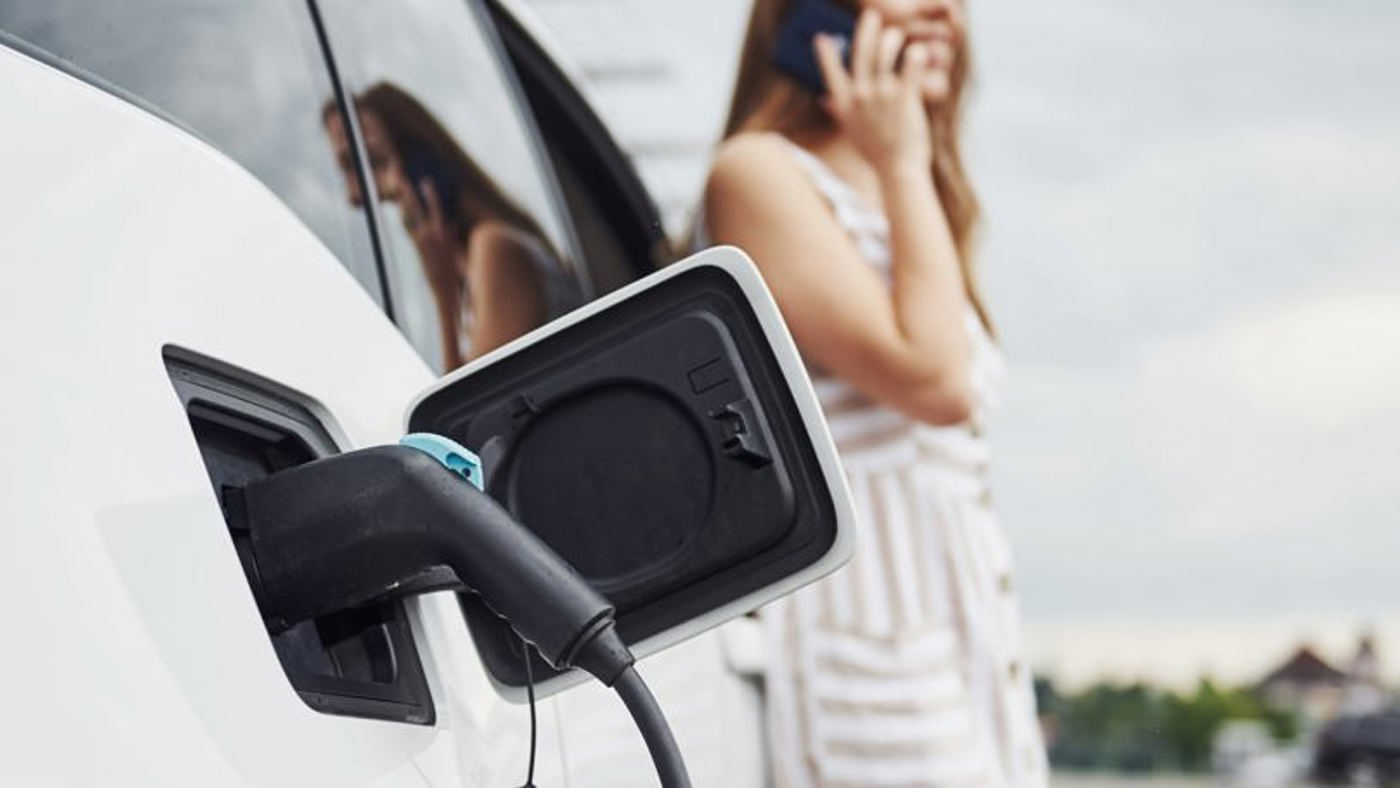 Woman talking on the phone whilst leaning against her electric car.